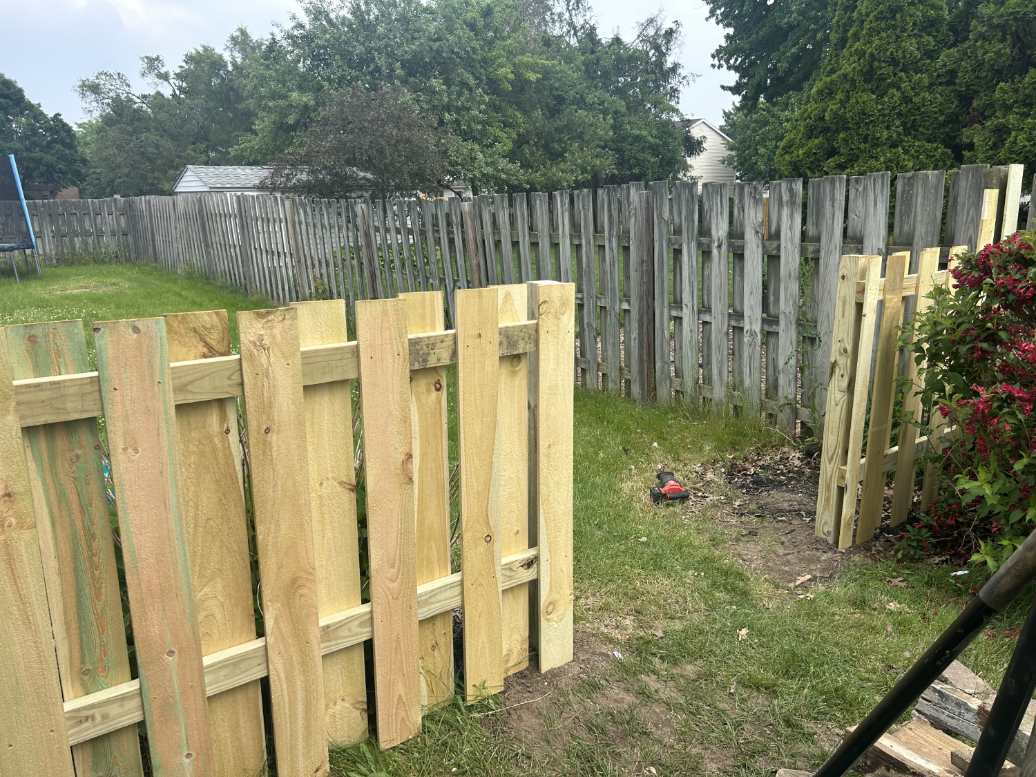 Close-up of a new light-colored wooden fence being built in a backyard