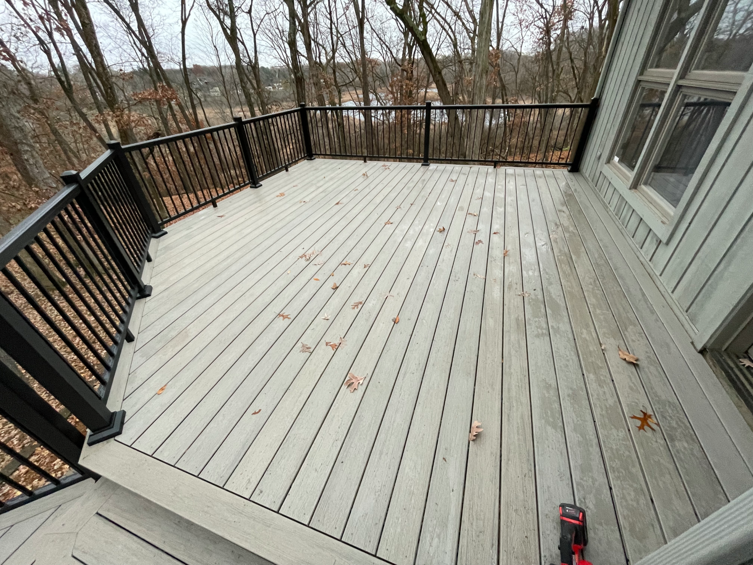 Wide-angle view of a clean, light-colored wooden deck with black railings overlooking woods